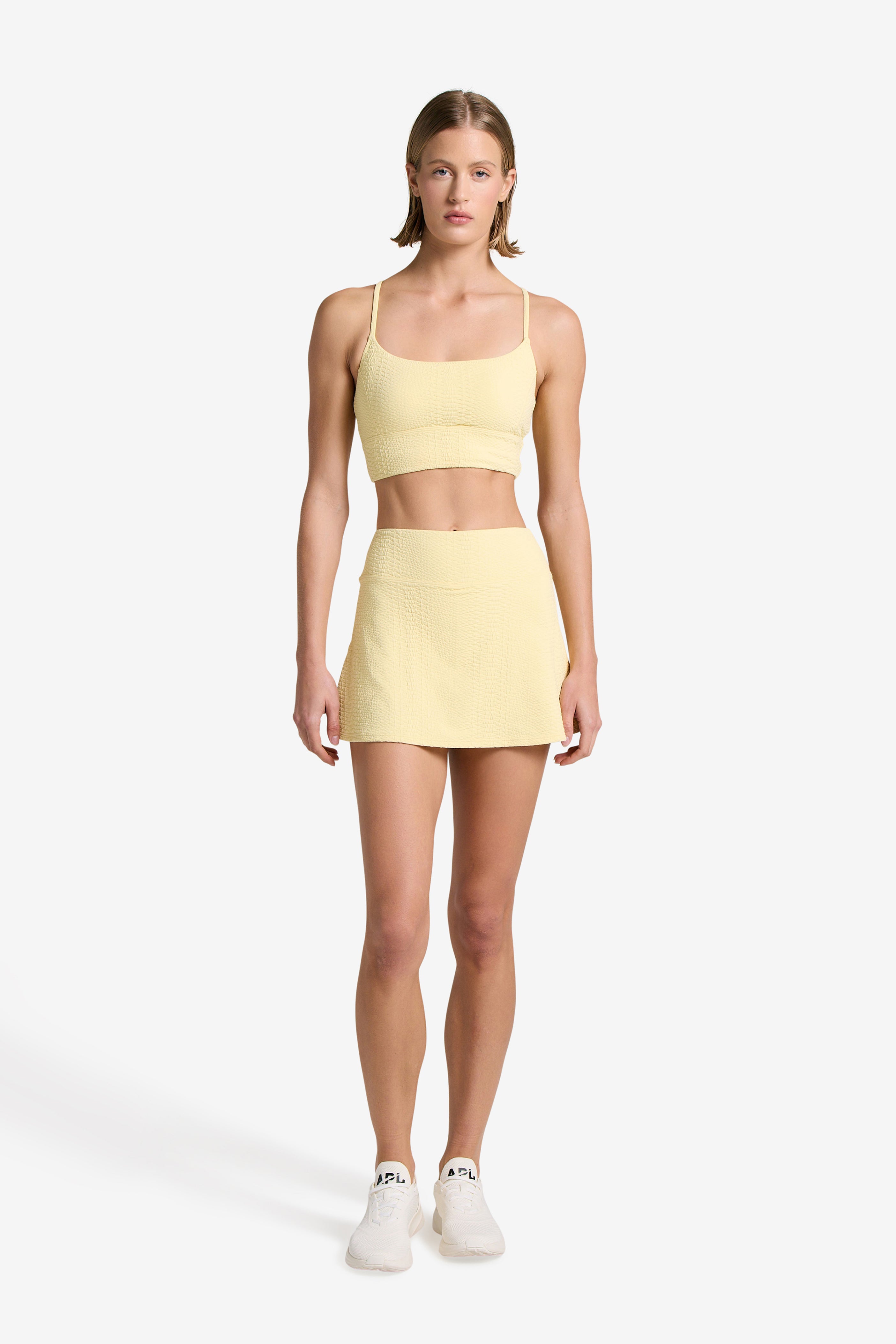 A woman faces forward in a Gigi C Sport Heidi Snakeskin Skort with built-in shorts and a matching crop top, paired with white sneakers. Her short hair is simply styled as she poses against a plain white background.